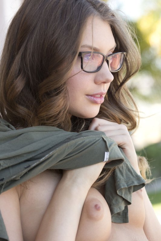 Молодая девушка в очках сексуально позирует во дворе